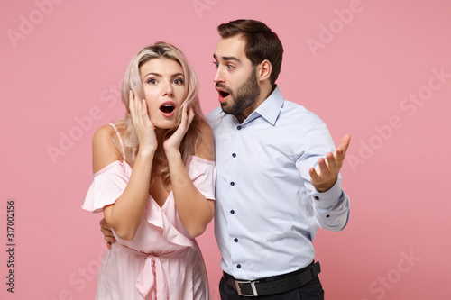 Shocked young couple two guy girl in party outfit celebrating posing isolated on pastel pink background. Valentine's Day Women's Day birthday holiday concept. Put hands on cheeks point hand on camera.