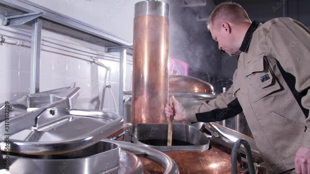 Small business and manufacturing concept. Male worker brews beer at the brewery Small business and manufacturing concept. Male worker brews beer at the brewery