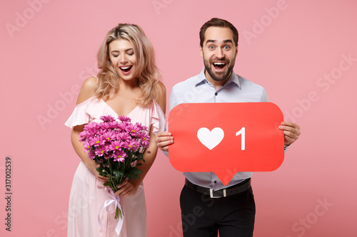 Couple two guy girl in party outfit celebrating isolated on pink background. Valentine's Day, Women's Day, birthday holiday concept. Hold huge like sign from Instagram heart form bouquet of flowers.