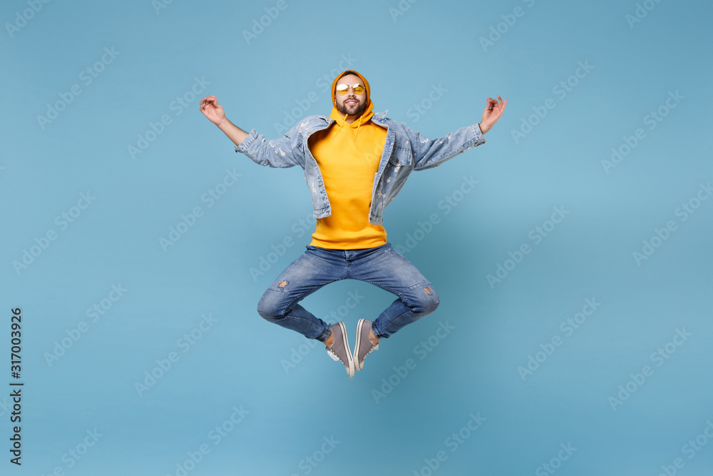 Relaxed young hipster guy in fashion jeans denim clothes posing isolated on pastel blue background. People lifestyle concept. Mock up copy space. Jump hold hands in yoga gesture, relaxing meditating. Relaxed young hipster guy in fashion jeans denim clothes posing isolated on pastel blue background. People lifestyle concept. Mock up copy space. Jump hold hands in yoga gesture, relaxing meditating.