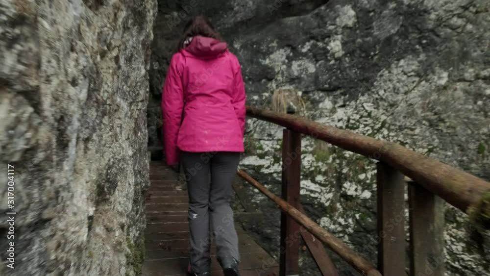 Camera following a lady walking a wooden path in a gorge. Huge drop off either side with wooden railing in hiking clothes. Pokljuka Gorge in Slovenia Triglav National Park. Camera following a lady walking a wooden path in a gorge. Huge drop off either side with wooden railing in hiking clothes. Pokljuka Gorge in Slovenia Triglav National Park.