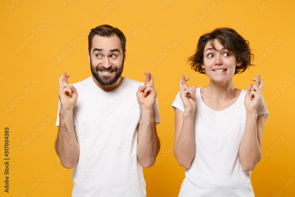 Young couple friends bearded guy girl in white t-shirts isolated on yellow orange background. People lifestyle concept. Mock up copy space. Wait for special moment keeping fingers crossed making wish. Young couple friends bearded guy girl in white t-shirts isolated on yellow orange background. People lifestyle concept. Mock up copy space. Wait for special moment keeping fingers crossed making wish.