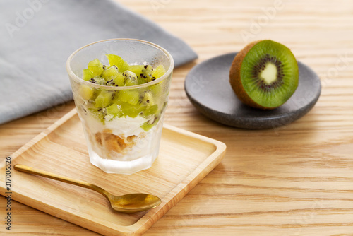 Kiwi parfait dessert with kiwi fruit, yogurt and crumble in a wooden plate with a golden spoon over a natural oak wooden background with grey napkin.