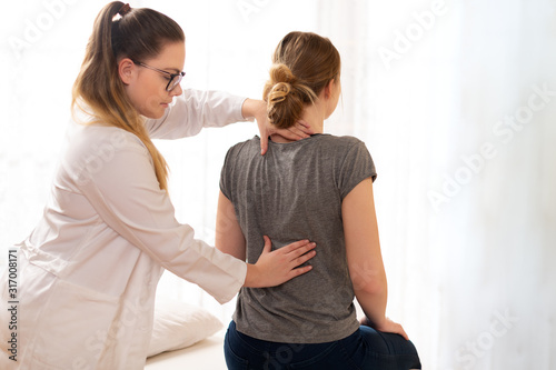 Female physiotherapist or a chiropractor examining patients back. Physiotherapy, rehabilitation concept.