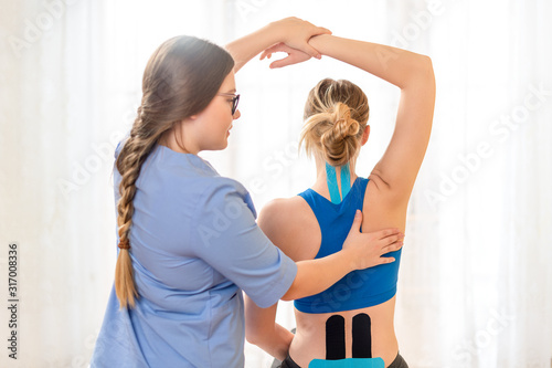 Young female patient wearing kinesio tape on her back and neck exercising with a professional physical therapist. Kinesiology, physical therapy, rehabilitation concept. photo