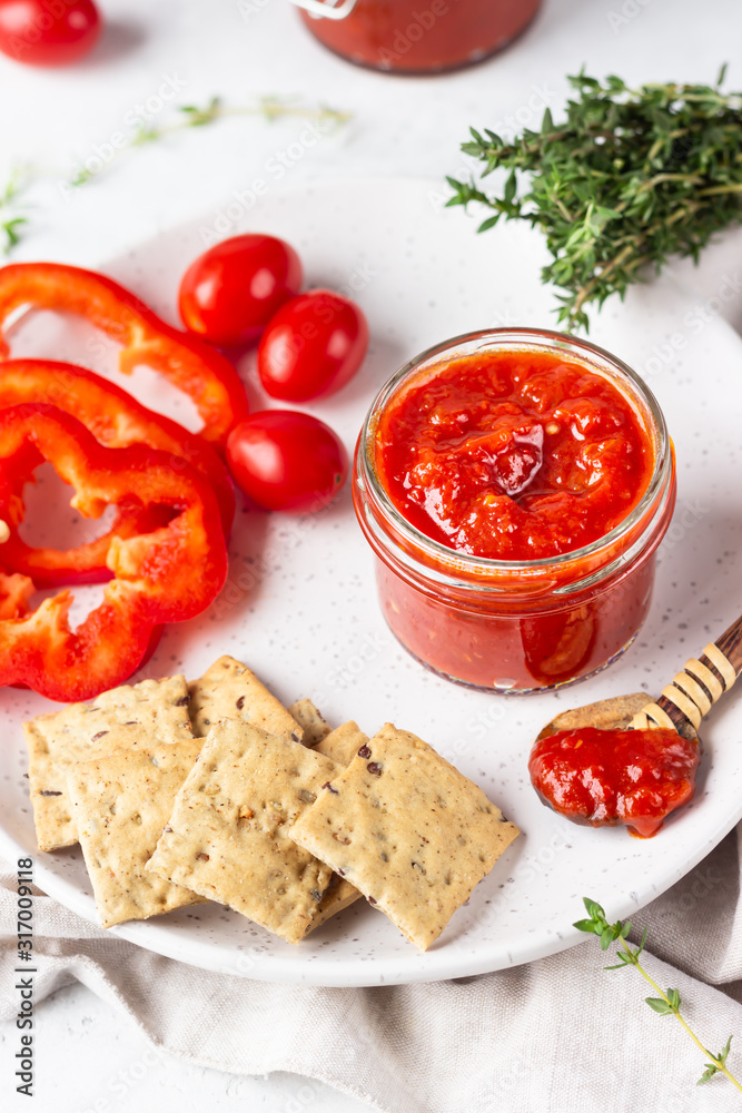 Ajvar (pepper mousse) or pindjur red vegetable spread made from paprika and tomatoes in glass jar on light stone table. Serbian native food. Ajvar (pepper mousse) or pindjur red vegetable spread made from paprika and tomatoes in glass jar on light stone table. Serbian native food.