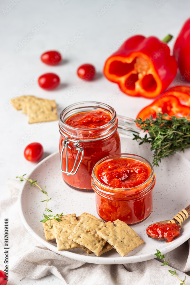 Ajvar (pepper mousse) or pindjur red vegetable spread made from paprika and tomatoes in glass jar on light stone table. Serbian native food. Ajvar (pepper mousse) or pindjur red vegetable spread made from paprika and tomatoes in glass jar on light stone table. Serbian native food.