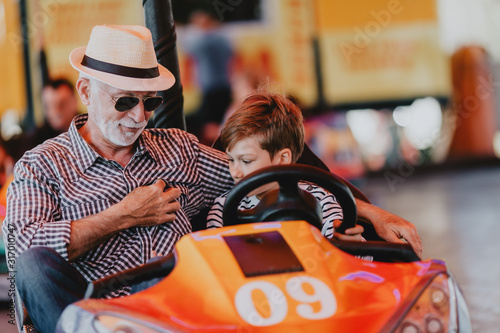 Grandfather and grandson having fun and spending good quality time together in amusement park. They enjoying and smiling while driving bumper car together.