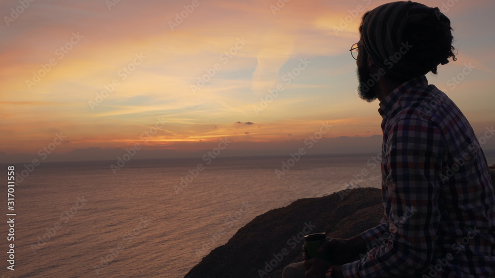 Handsome middle eastern male sitting on a cliff at sunrise