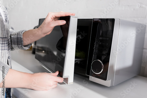 cropped view of woman closing door of microwave in kitchen