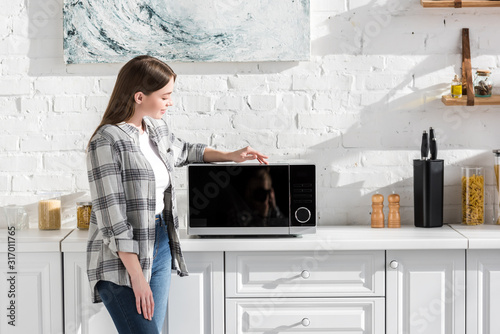 smiling woman in shirt looking at microwave in kitchen photo