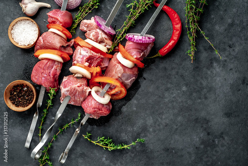 Raw skewers of meat. Barbecue meat with vegetables and spices on a stone background. Free space for your text.