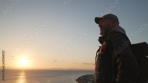 Handsome senior traveler with selfie stick climb up a hill at sunrise