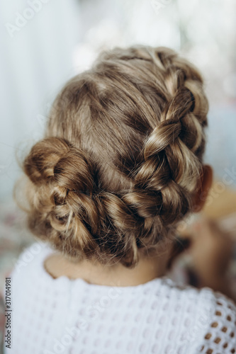 Festive hairstyle from braid on a child girl with long hair, back view.