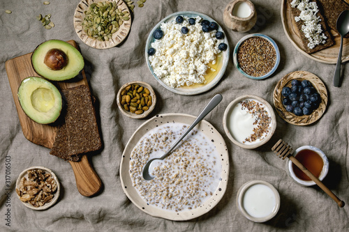 Healthy breakfast. Variety of breakfast dishes sprouted wheat, yogurt, kefir, cottage cheese, avocado, rye bread, seeds, nuts and berries assortment in ceramic bowls. Linen cloth background. Flat lay