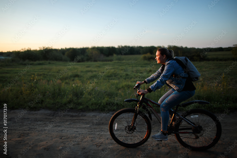 A woman rides her bike on a field road at sunset.