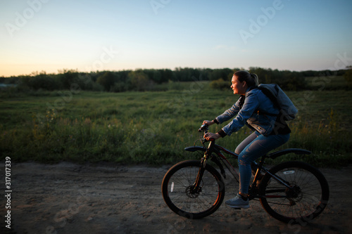 A woman rides her bike on a field road at sunset.