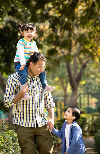 Father carrying daughter on shoulders and holding hands of his son at park