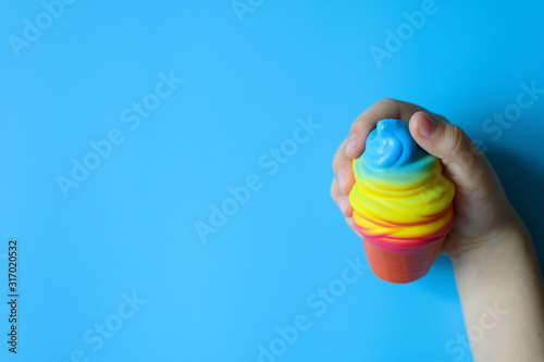 anti stress squishy toy in the form of multicolored ice cream in children's hands on blue background. space for text © Ksenia