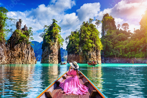 Beautiful girl sitting on the boat and looking to mountains in Ratchaprapha Dam at Khao Sok National Park, Surat Thani Province, Thailand. photo