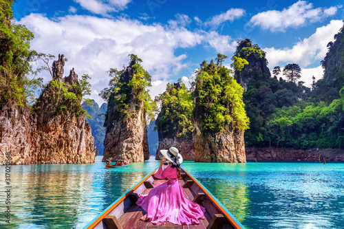 Beautiful girl sitting on the boat and looking to mountains in Ratchaprapha Dam at Khao Sok National Park, Surat Thani Province, Thailand.