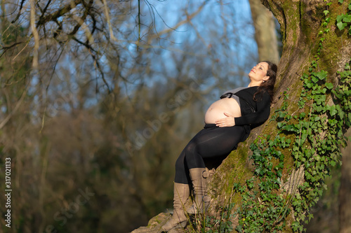 Pregnant woman leaning back on the tree