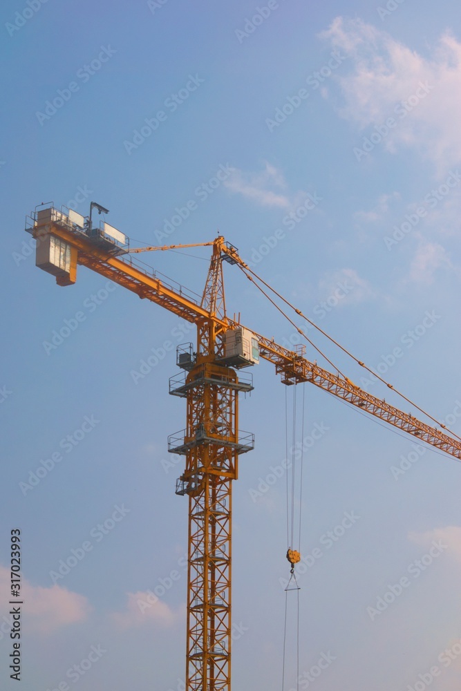 Yellow construction tower crane against a clear blue sky. Low angle shot.