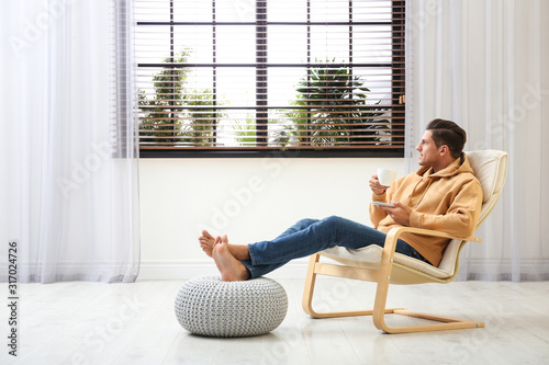 Attractive man relaxing in armchair near window at home. Space for text