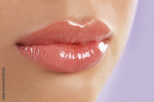 Young woman with beautiful full lips on lilac background, closeup