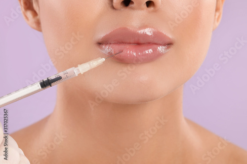 Young woman getting lips injection on lilac background  closeup