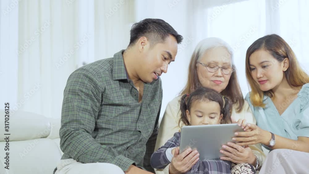 Three generation family using a digital tablet while sitting together on the sofa at home. Shot in 4k resolution Three generation family using a digital tablet while sitting together on the sofa at home. Shot in 4k resolution
