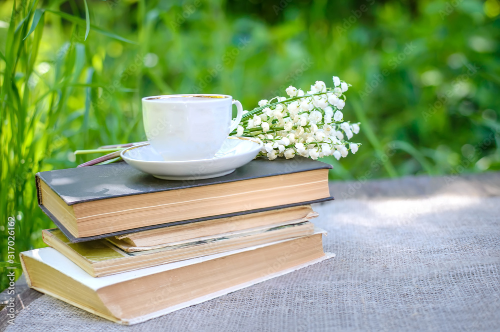 Spring flowers lilies of the valley and a cup of tea on a stack of old books