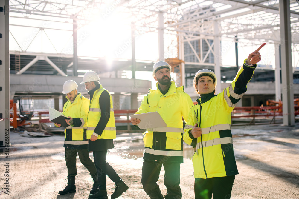 Group of engineers standing outdoors on construction site, working. - obrazy, fototapety, plakaty 