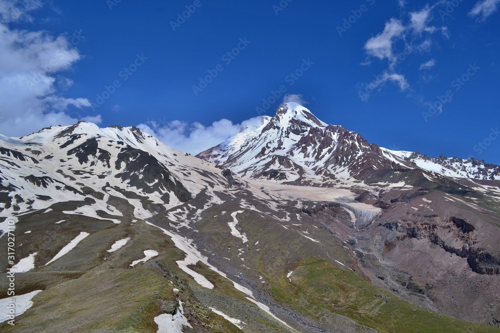 Beautiful impozant Kazbek mountain  covered with glacier, Georgia. Sunny day, blue sky with white clouds.