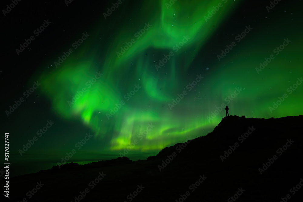 A man stands on a mountain and looks at the northern lights A man stands on a mountain and looks at the northern lights