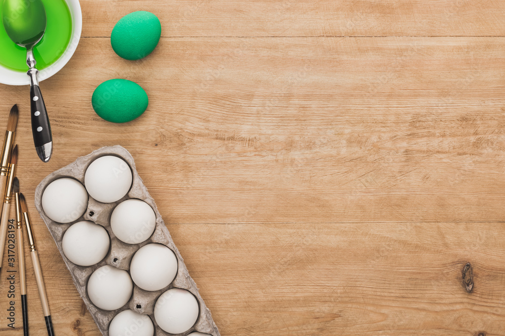 top view of green watercolor paint in bowl near chicken eggs and paintbrushes on wooden table top view of green watercolor paint in bowl near chicken eggs and paintbrushes on wooden table