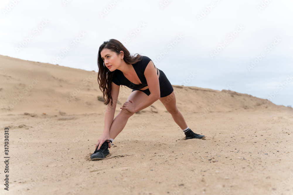 Beautiful long hair latin brunette fitness model wearing black short fitness outfit exercising and stretching in the Middle East desert  sands