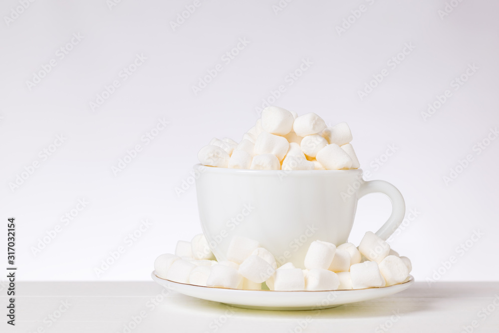 Small pieces of marshmallow in a white Cup and saucer on a white table. Small pieces of marshmallow in a white Cup and saucer on a white table.