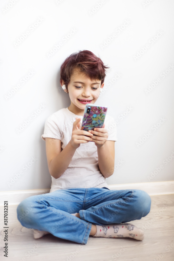 Vertical full length portrait little short haired schoolgirl with pink hair listening music and looking on mobile phone with white wireless headphones. Smart lifestyle. Gadget addicted childhood Vertical full length portrait little short haired schoolgirl with pink hair listening music and looking on mobile phone with white wireless headphones. Smart lifestyle. Gadget addicted childhood