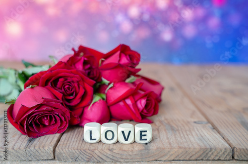 Love sign on wooden cubes and red roses flower on wooden table. Love and Valentine day concept.