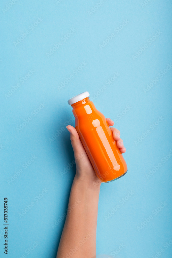Φωτογραφία A bottle of orange juice or detox drink in a woman's hand over blue