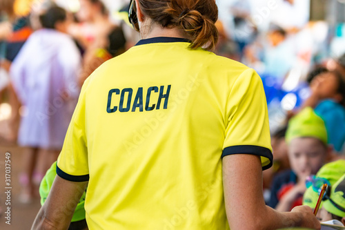 Back view of a female coach wearing bright green coach shirt with the word COACH printed on back