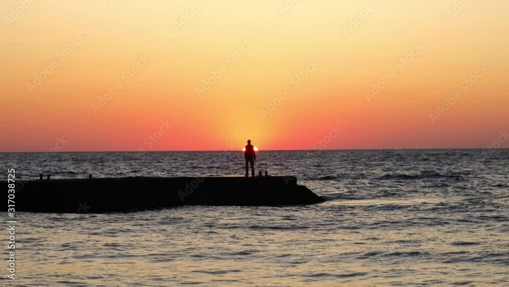 A lonely man at sunrise. A man on the beach meets the dawn. sea wave A lonely man at sunrise. A man on the beach meets the dawn. sea wave