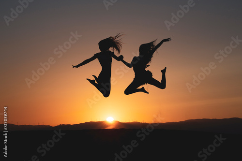 Jóvenes amigas saltando con alegría al atardecer en contraluz © Sinu Mora