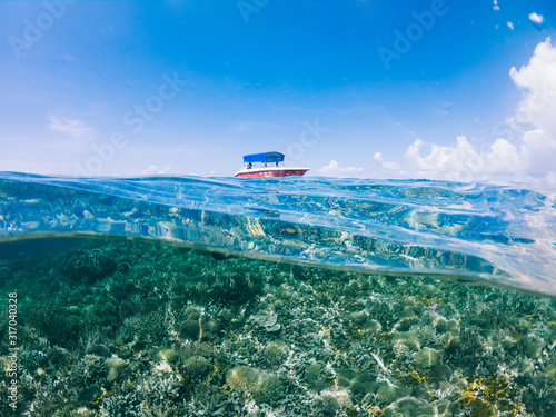 Surface landscape of picturesque horizontal split shot of small motor boat during getaway travel trip to marine lagoon with crystal clear water and coral reefs in depth, concept of ocean tourism