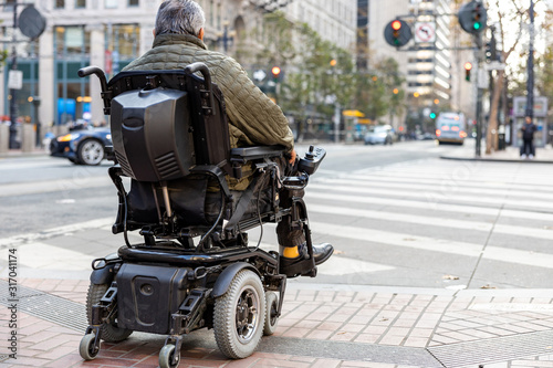An elderly disabled person on an electric wheelchair on a city street in front of a pedestrian crossing. The concept of modern technology for people with disabilities. photo