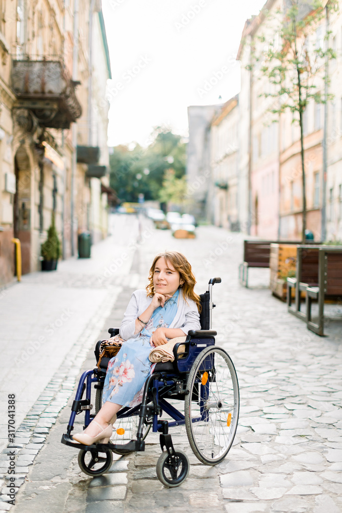 attractive disabled blond young girl in blue dress sitting in a wheelchair, outdoors in the city
