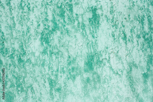 Shabby old fence covered faded green paint with light smudges on stucco. Vintage background for your design. Abstract grunge texture of peeling paint on worn wall.