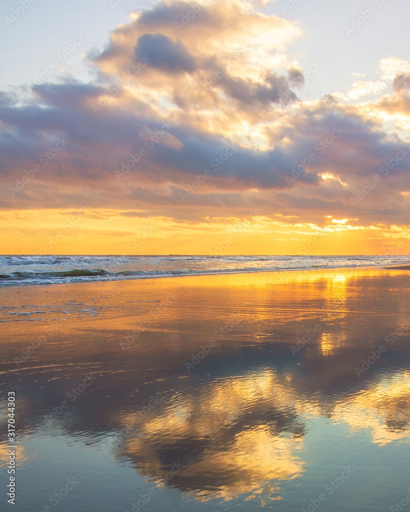 Beautiful warm golden sunlit clouds during sunset perfectly reflecting in the sand on a beach. Fire Island National Seashore - New York