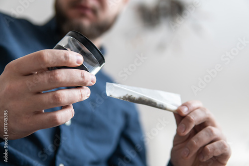 Preparing a joint and drug paraphernalia concept theme with close up man hands rolling a joint with herb girder to grind a cannabis buds in the background